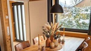 Une table à manger en bois, accompagnée de chaises, d’un luminaire suspendu et d’objets décoratifs.