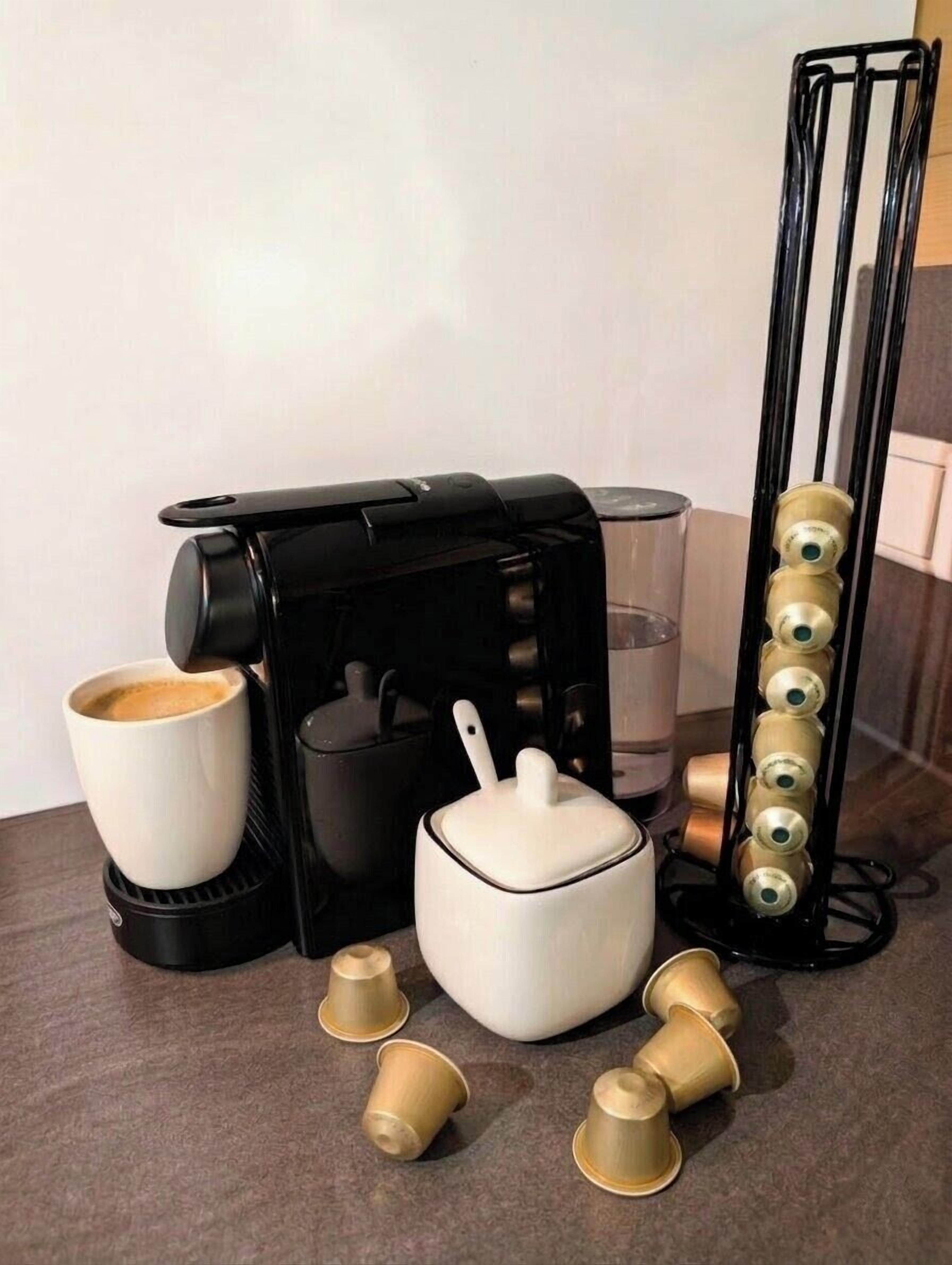 A coffee maker, a white mug, a glass, and a coffee pod holder on a kitchen counter.
