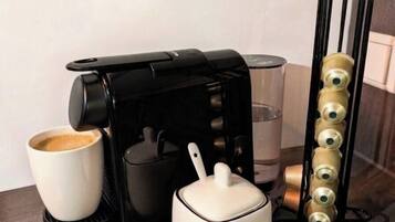 A coffee maker, a white mug, a glass, and a coffee pod holder on a kitchen counter.