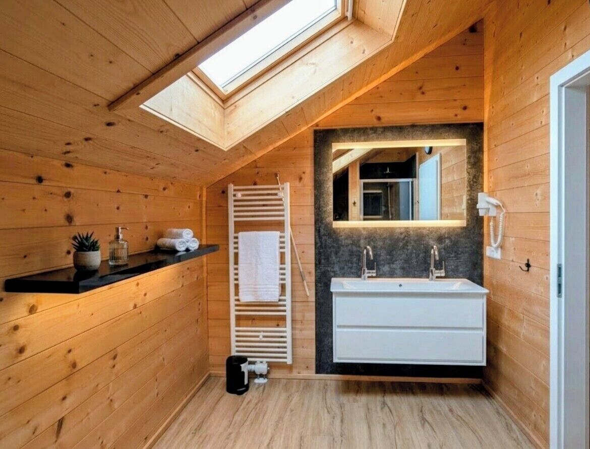 A wooden cabin bathroom with a skylight, a white sink, and a towel rack.