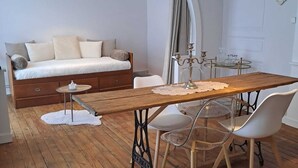 A room with a wooden dining table, white chairs, a sofa bed, a small round table with a candle, and a black pendant light. - Appart l'Elégant in the historic center of Saumur (Saumur)