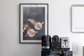Ein gerahmtes Kunstwerk mit Kaffeetassen an einer Wand, eine Kaffeemaschine und ein Toaster auf einer Arbeitsfläche.