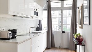 Moderni keittiö, jossa on valkoiset kaapit, sisäänrakennettu mikroaaltouuni, leivänpaahdin ja pesuallas.