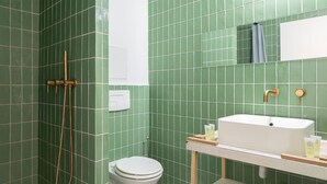 Kylpyhuoneessa on vihreät laatat, valkoinen pesuallas, wc ja suihku, jossa on kullanvärinen hana.