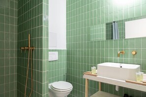 Ein Badezimmer mit grünen Fliesen, einem weißen Waschbecken, einer Toilette und einer Dusche mit goldenem Wasserhahn.