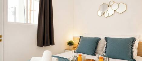 A neatly made bed with blue bedding, a tray with breakfast items, and a wall-mounted hexagonal mirror.