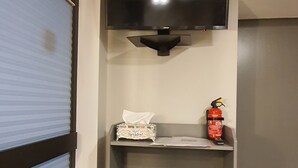 A room with a grey storage unit, a mounted flat-screen TV, a fire extinguisher, and a blue shuttered window. - Quiet apartment with garden & terrace, parking space (Neuss)