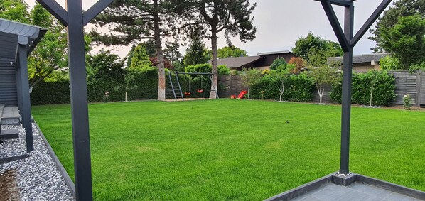 A backyard with a well-maintained lawn, a swing set, and a slide.