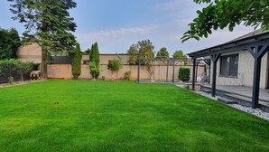 A well-maintained backyard with a lawn, a brick wall, and a covered patio area. - Quiet apartment with garden & terrace, parking space (Neuss)