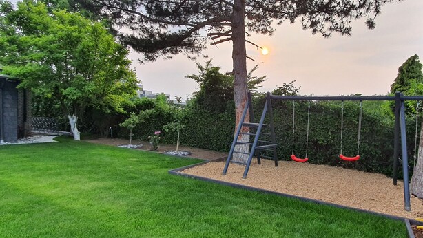 A playground with swings and a ladder, surrounded by a well-maintained lawn and trees. - Quiet apartment with garden & terrace, parking space (Neuss)