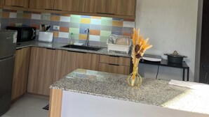 Uma cozinha moderna com armários de madeira, bancada de granito, pia, micro-ondas e um vaso decorativo com espigas de trigo.