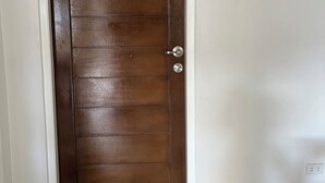 Uma porta de madeira fechada com puxador prateado, moldura branca e um tapete cinza sobre piso de azulejos.