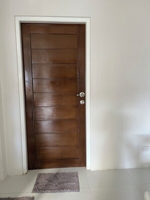 Una puerta de madera cerrada con un picaporte plateado, un marco blanco y una alfombra gris sobre un suelo de baldosas.