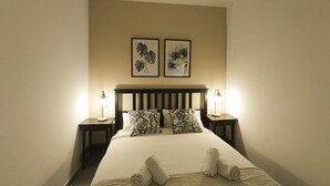 A hotel room with a bed, two nightstands, two wall-mounted lamps, and two framed botanical prints. - Santa Cruz Holiday Home (Santa Cruz de Tenerife)