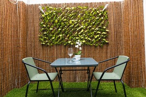 Cercado de bambu com folhagem verde, mesa de vidro, duas cadeiras e um vaso de planta.