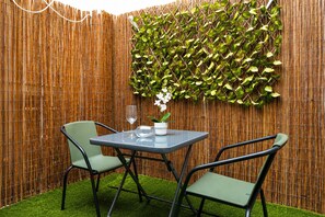 A small outdoor seating area with a table and two chairs, a bamboo fence, and a wall covered with green foliage. - Santa Cruz Holiday Home · 2 Bedrooms & Patio (Santa Cruz de Tenerife)