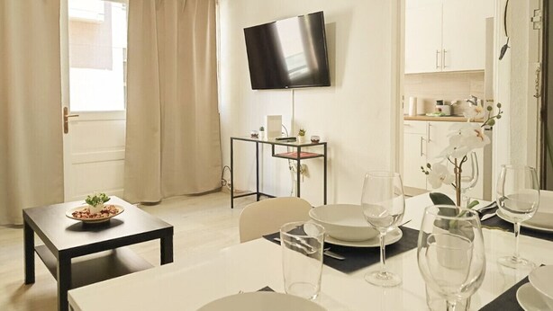 A dining area with a table set for two, a TV mounted on the wall, and a kitchen in the background. - Santa Cruz Holiday Home (Santa Cruz de Tenerife)