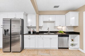 A modern kitchen with white cabinetry, stainless steel appliances, and a black countertop. - 4BR/4BA Tampa Retreat | Game Room & Patio (Tampa)