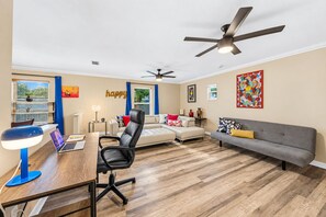 A modern living room with a desk, office chair, sofa, and two ceiling fans. - 4BR/4BA Tampa Retreat | Game Room & Patio (Tampa)
