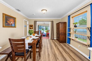 A dining area with a wooden table set for four, a large cabinet, and a view of the outdoors through a window with blinds. - 4BR/4BA Tampa Retreat | Game Room & Patio (Tampa)