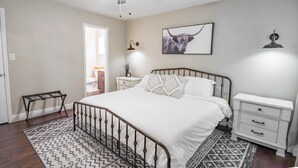A bedroom with a bed, bedside tables, a ceiling fan, a rug, and a framed picture on the wall.