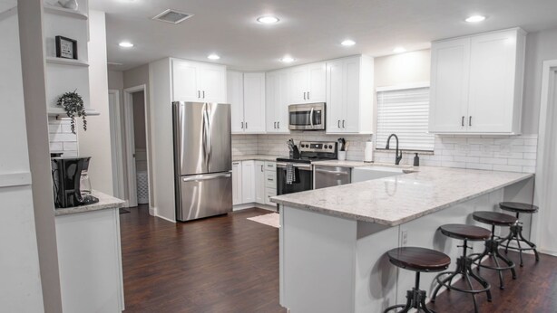 A modern kitchen with white cabinetry, stainless steel appliances, and a central island with bar stools.