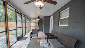 A covered patio with wicker furniture, a ceiling fan, and large windows.