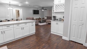 A modern kitchen with white cabinetry, a dining area with a table and chairs, and a living room with a sofa and a coffee table.