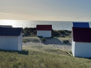 Een strand met drie kleine strandhutjes, een zandpad en de oceaan op de achtergrond.