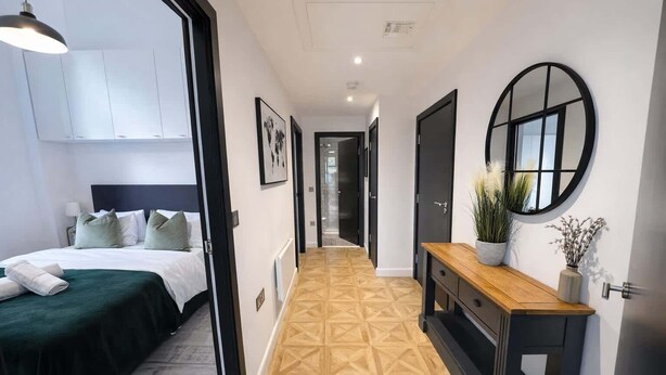 Habitación de hotel con cama, mesita de noche con un florero, espejo y pasillo con piso de diseño geométrico.