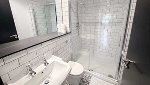 Un baño moderno con cabina de ducha de vidrio, un lavabo blanco con dos grifos y un inodoro.