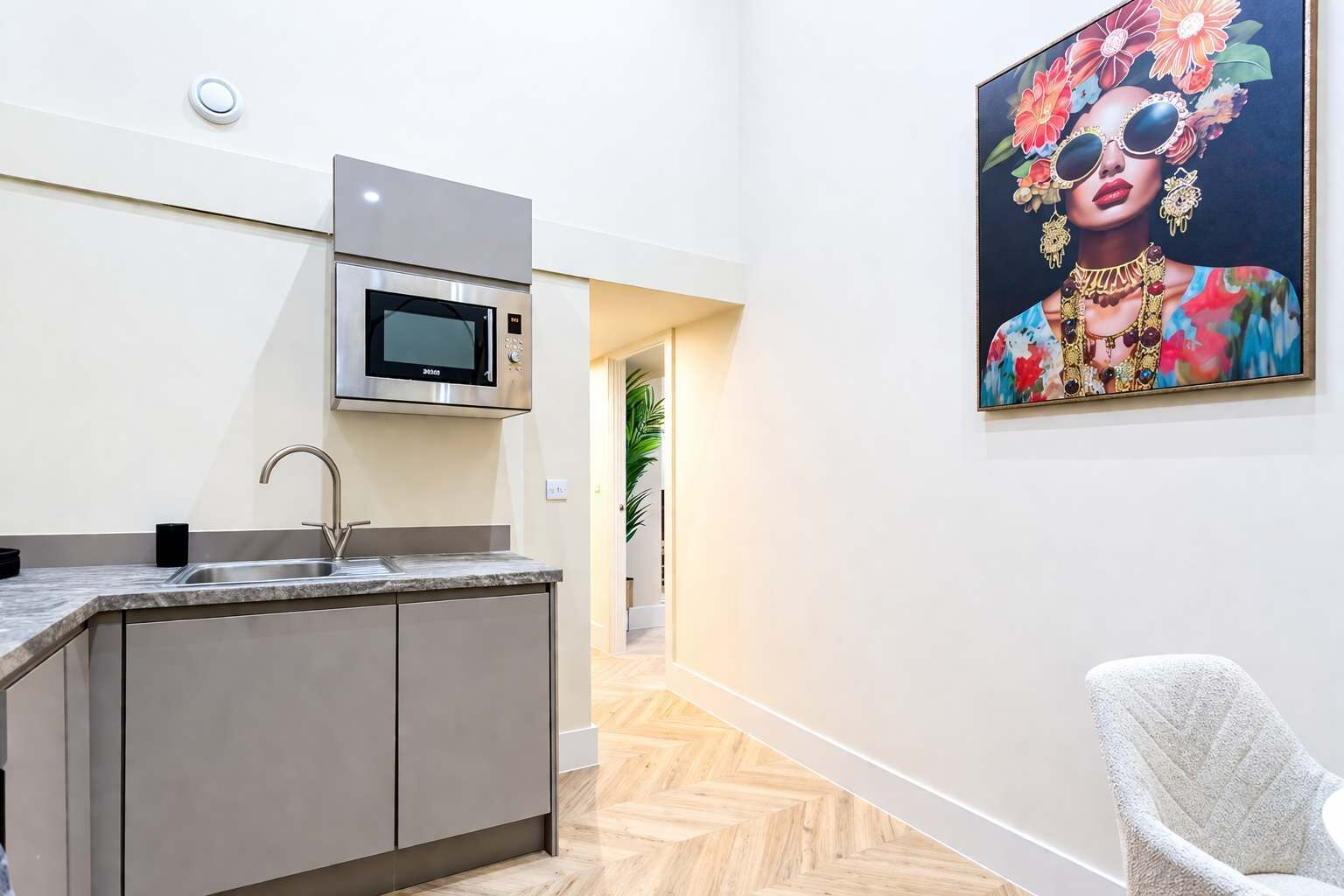Una cocina moderna con microondas, pileta y muebles, un pasillo con una puerta y un cuadro en la pared.