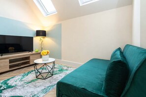 A modern living room with a flat-screen TV, a round coffee table with a vase of flowers, a teal sofa, and a geometric-patterned rug. - Modern Executive 1BR Leeds City Centre Apartment (West Yorkshire)
