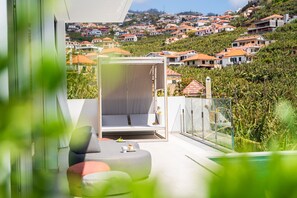A modern outdoor seating area with a view of a hillside residential area. - Heated Infinity Pool • Cinema Room • Sea Views (Ponta do Sol)