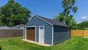 A blue shed with a door and a window, surrounded by a wooden fence and grass. - Cute Newly Remodeled Home Close to Notredame 2bed (Mishawaka)