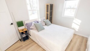 A bedroom with a bed, a nightstand, a window, and a door. - Cute Newly Remodeled Home Close to Notredame 2bed (Mishawaka)