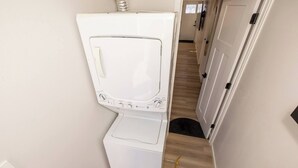 A compact laundry room with a front-loading washer and dryer, a wooden floor, and a door leading to another room. - Cute Newly Remodeled Home Close to Notredame 2bed (Mishawaka)