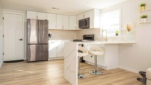 A modern kitchen with white cabinets, stainless steel appliances, a microwave, and a bar area with stools. - Cute Newly Remodeled Home Close to Notredame 2bed (Mishawaka)
