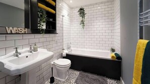 Un baño con paredes de azulejos blancos, una bañera negra, un lavabo blanco y un inodoro.