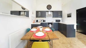 Una cocina moderna con armarios oscuros, una mesa de comedor de madera con individuales rojos e iluminación colgante.