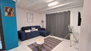 A living room with a blue sofa, a patterned rug, a small round table, and a standing fan. - T2 neuf au Gosier - close to beaches - quiet & central, ideal for vacations (Le Gosier)