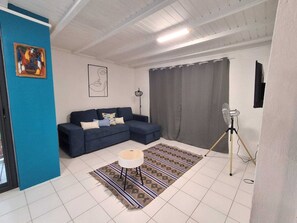 Ein Wohnzimmer mit einem blauen Sofa, einem gemusterten Teppich, einem kleinen runden Tisch und einem Standventilator.