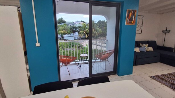 A room with a sliding glass door leading to a balcony, a dining table with chairs, a sofa, and a floor lamp. - T2 neuf au Gosier - close to beaches - quiet & central, ideal for vacations (Le Gosier)