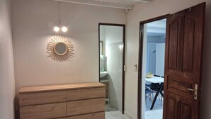 A hallway with a wooden dresser, a sunburst mirror, and a door leading to a bathroom. - T2 neuf au Gosier - close to beaches - quiet & central, ideal for vacations (Le Gosier)
