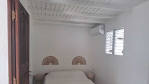 A bedroom with a wooden bed, two wall-mounted fans, a window with blinds, and an air conditioning unit. - T2 neuf au Gosier - close to beaches - quiet & central, ideal for vacations (Le Gosier)