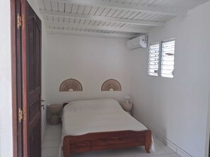 Ein Schlafzimmer mit einem hölzernen Bett, zwei Wandventilatoren, einem Fenster mit Jalousien und einer Klimaanlage.