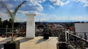Eine Dachterrasse mit Blick auf eine Stadtlandschaft, einer Palme und einer weißen Säule.