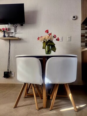 A dining area with a round table, two white chairs, a vase with flowers, a wall-mounted TV, and a power outlet. - Residential Apartment with Gym, Coworking and more.Zona Tepeyac Basilica Guadalupe (Ciudad de México)