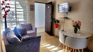 Ein Wohnzimmer mit einer Couch, einem Esstisch, einem Fernseher und einer Tür zu einem weiteren Raum.