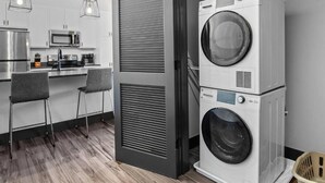 Una cocina compacta con microondas, cafetera y lavabo. Hay dos taburetes de bar y una lavadora.